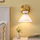 A transitional bedroom features the Cori Wall Sconce, Brushed Brass and Milk Glass mounted above a nightstand displaying a ceramic vase of daisies.