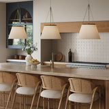 Modern kitchen with three Adrian 18" Pendant lights in Antique Brass, hung above a stone island, with wicker chairs.