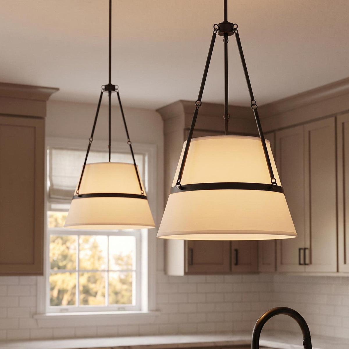 A transitional kitchen features two Julien Pendant 18", Matte Black fixtures with fabric shades hanging above a counter near greige shaker cabinets and subway tile.