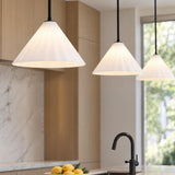 A modern kitchen featuring three white fluted glass cone pendants with matte black stems suspended over a marble island with light wood cabinetry and a black faucet.