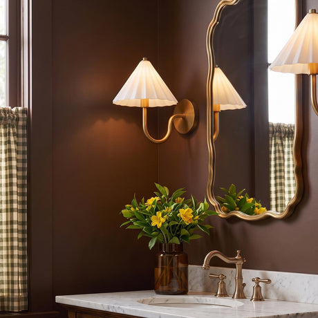 A traditional bathroom featuring the Reese Wall Sconce, Aged Brass and Opal Glass mounted on brown walls beside a brass scalloped mirror and marble vanity.