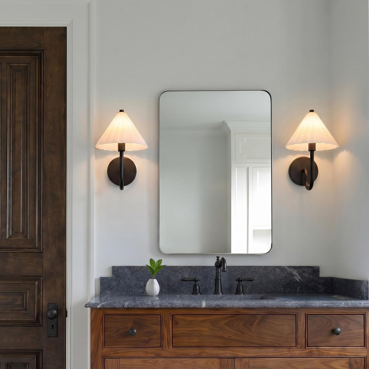 A transitional bathroom with two Reese Wall Sconce, Matte Black and Opal Glass fixtures flanking a rectangular mirror above a dark wood vanity with a gray stone countertop.