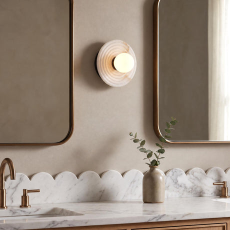 A transitional bathroom features a Bren LED Wall Sconce, Urban Bronze and Alabaster, mounted between two bronze framed mirrors over a scalloped marble vanity.