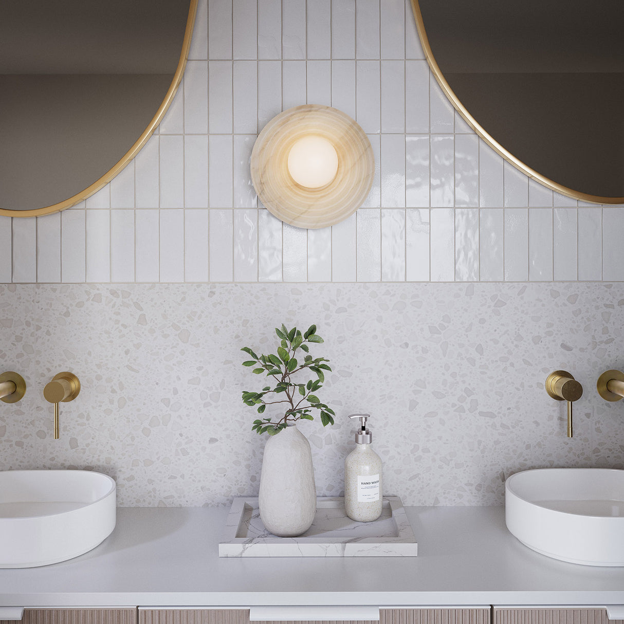 Modern bright bathroom with two round mirrors, the Bren single wall sconce in the center, and a decorative plant on a countertop.