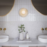 Modern bright bathroom with two round mirrors, the Bren single wall sconce in the center, and a decorative plant on a countertop.