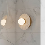 Bren LED Wall Sconce, Vintage Brass and Alabaster - A single sconce is mounted on a marble wall, its reflection visible in a nearby mirror.