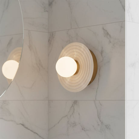 Bren LED Wall Sconce, Vintage Brass and Alabaster - A single sconce is mounted on a marble wall, its reflection visible in a nearby mirror.