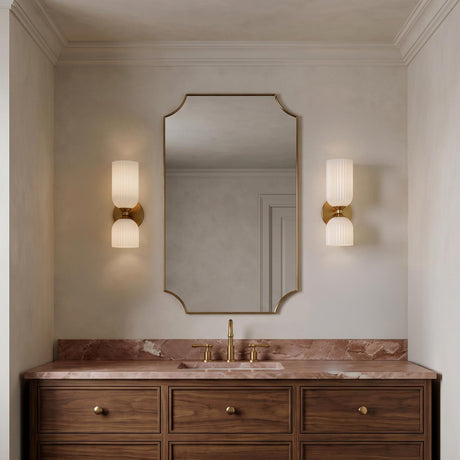 A transitional bathroom featuring two Elle Wall Sconce, Brushed Brass and Milk Glass fixtures flanking a scalloped mirror over a pink marble countertop and walnut vanity.