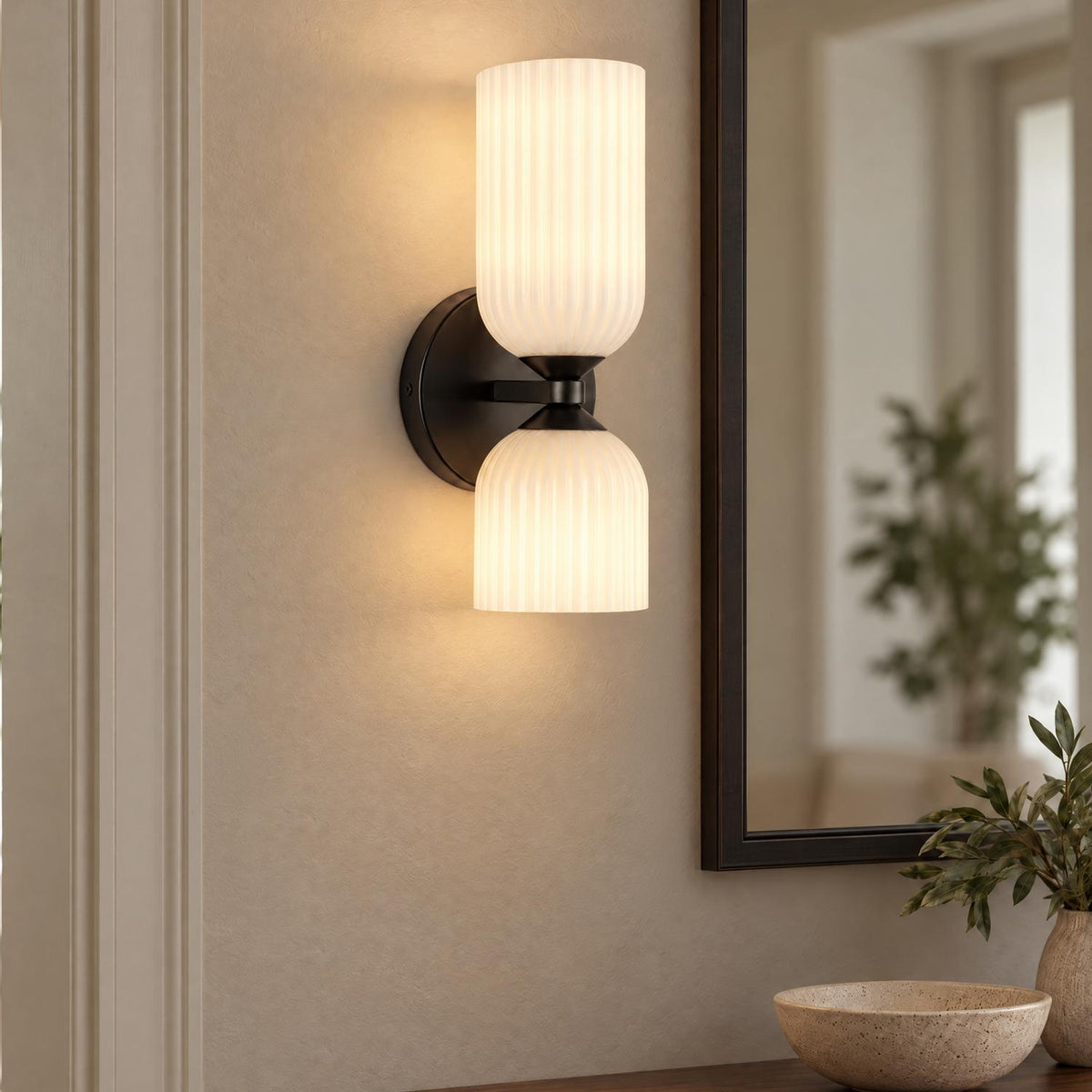 A transitional foyer featuring an Elle Wall Sconce, Matte Black and Milk Glass beside a dark framed mirror above a wooden console table with ceramic decor.
