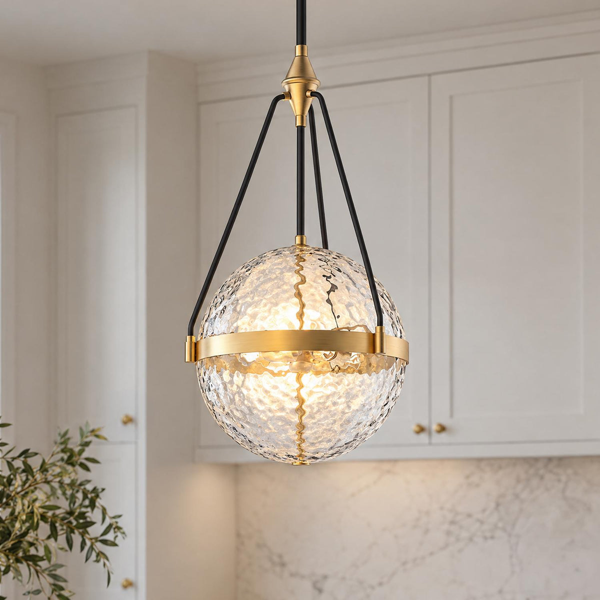 A transitional kitchen features the Darcy Large Pendant 18", Brushed Brass and Water Glass hanging in front of off-white shaker cabinetry and a white marble backsplash.