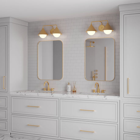 Double bathroom vanity showcasing Juno 2 Light wall sconces above the mirrors, finished in aged brass with white opal glass globes. The bathroom is contemporary, light grey with brass hardware, and with white marble countertops.