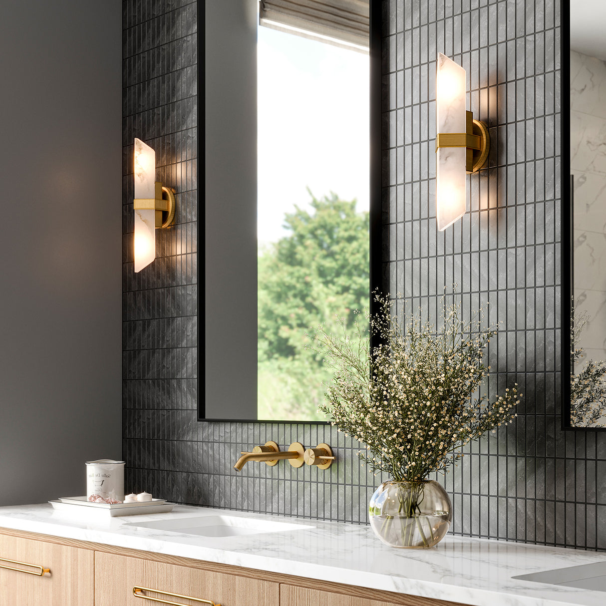 Gracy 2 Light Wall Sconce, Vintage Brass and real Alabaster stone wall sconces are shown in a primary bathroom flanking large black mirrors with dark grey stone tile backsplash.
