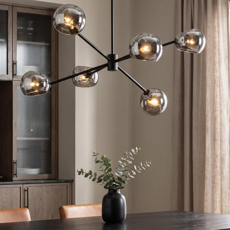A modern dining room features a Flynn 6 Light Chandelier 37", Matte Black with Mirrored Smoke Glass suspended over a dark wood table with tan leather chairs.