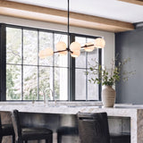 A modern kitchen featuring the Flynn 8 Light Linear Pendant in matte black with opal glass globes suspended over a marble waterfall island with stools.