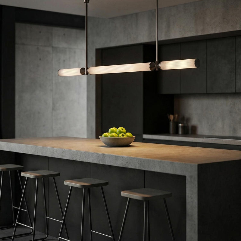 An industrial kitchen features the Blain LED Linear Pendant 48", Urban Bronze with ribbed glass over a concrete waterfall island surrounded by dark gray cabinetry.