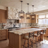 A transitional kitchen features three Pierce Small Lantern Pendants in Urban Bronze suspended over a heavily veined marble island with light wood cabinetry.