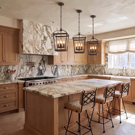 A transitional kitchen features three Pierce Small Lantern Pendants in Urban Bronze suspended over a heavily veined marble island with light wood cabinetry.
