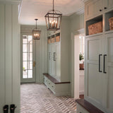 A modern farmhouse foyer with two Pierce Medium Lantern Pendants in urban bronze suspended over herringbone brick flooring and sage green mudroom cabinets with wood benches.