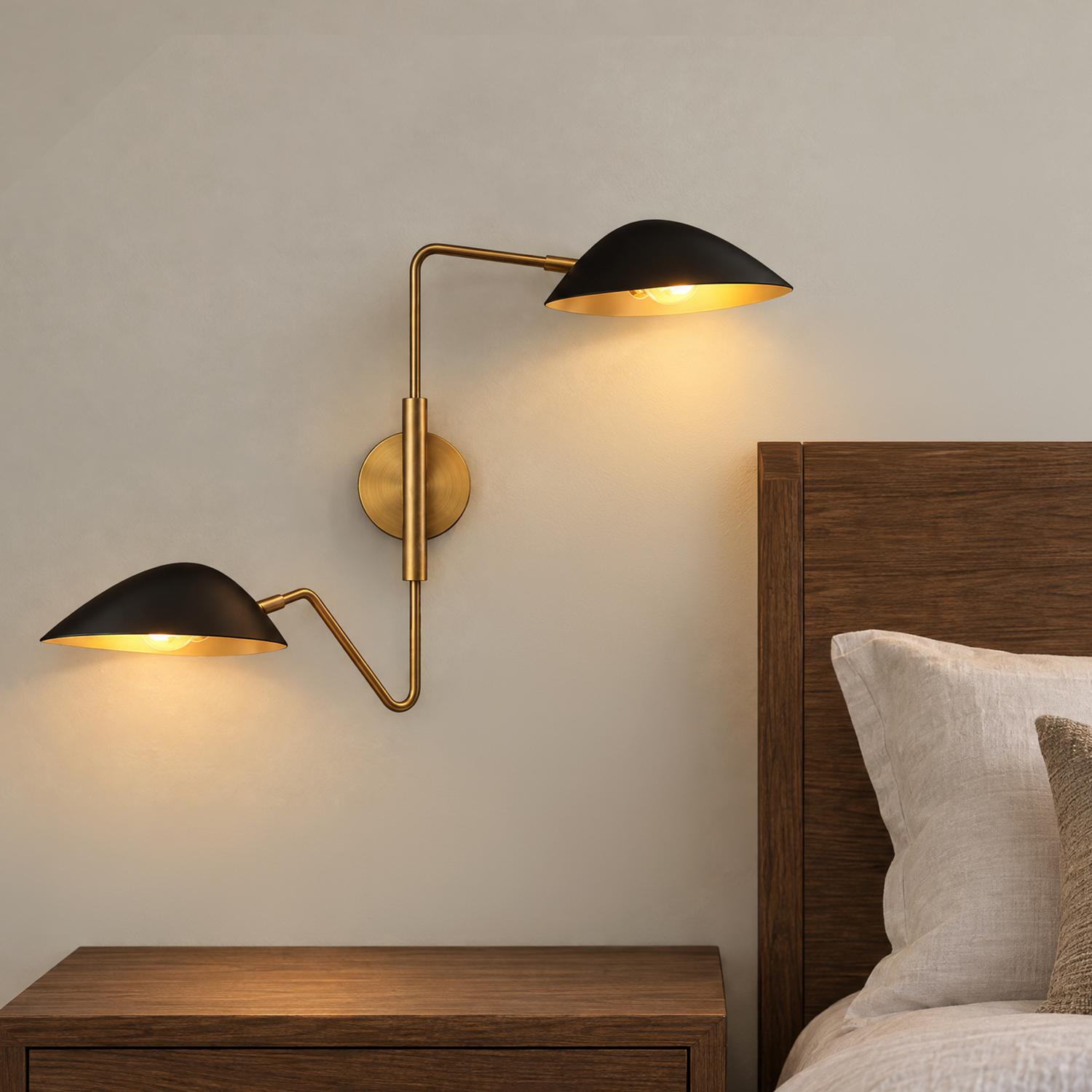 A mid-century modern bedroom featuring the Jade Double Swing Arm Sconce, Matte Black and Antique Brass mounted beside a dark wood headboard and nightstand.