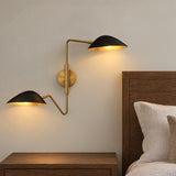 A mid-century modern bedroom featuring the Jade Double Swing Arm Sconce, Matte Black and Antique Brass mounted beside a dark wood headboard and nightstand.