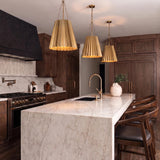 A transitional kitchen with three antique brass pleated pendants hanging over a white marble waterfall island surrounded by dark walnut cabinetry and a black range hood.