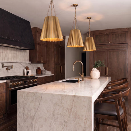 A transitional kitchen with three antique brass pleated pendants hanging over a white marble waterfall island surrounded by dark walnut cabinetry and a black range hood.