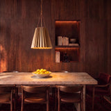 A mid-century dining room features the Maris Medium Pendant 16", Antique Brass suspended over a light stone dining table set against rich dark wood paneling.