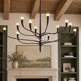 A transitional living room features an organic antique iron twelve-light chandelier suspended beneath a wooden beamed ceiling above a stone fireplace with green built-ins.