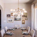 A transitional dining room features the Amara 9 Light Chandelier in gold leaf with art glass suspended over a wooden table before a framed gallery wall.