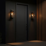 Two Orin Outdoor Small Wall Lights, Bronze with Vintage Brass Accents, shown at night on a dark grey modern facade with wood accent wall.