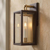 A transitional home exterior featuring the Orin Outdoor Wall Light in bronze with vintage brass accents mounted on a textured stone wall beside an entryway.