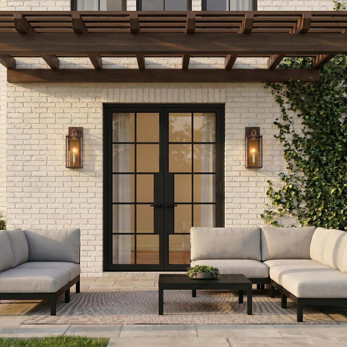 A modern farmhouse patio with two Orin Outdoor Wall Lights in bronze and vintage brass accents flanking black doors on white brick under a pergola at dusk.