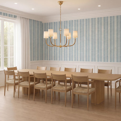 A transitional dining room with the Iris 6 Light Chandelier in aged brass with rattan over a light wood table and blue striped wallpaper with white wainscoting.