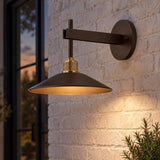 A modern farmhouse entry features the Emeri LED Outdoor Wall Light in bronze with vintage brass accents on a white brick wall beside a potted plant at dusk.