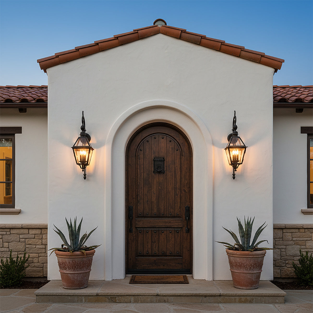 Ashford Outdoor Wall Light, Small 33" Black - Two black outdoor wall lights illuminate a rustic wooden arched doorway flanked by potted plants.