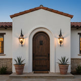 Ashford Outdoor Wall Light, Small 33" Black - Two black outdoor wall lights illuminate a rustic wooden arched doorway flanked by potted plants.