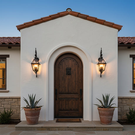 Ashford Outdoor Wall Light, Small 33" Black - Two black outdoor wall lights illuminate a rustic wooden arched doorway flanked by potted plants.