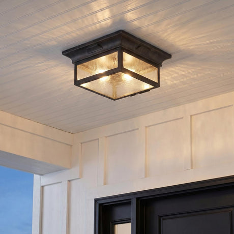 An outdoor entryway featuring the Bedford Outdoor Flush Mount, Antique Black Iron with seeded glass attached to a white beadboard ceiling above a black front door.