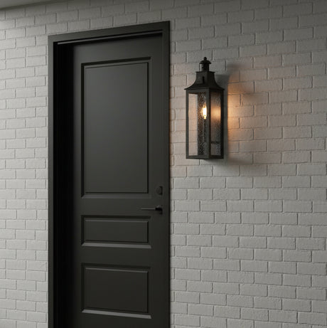 Bedford Outdoor Wall Light, Small 18" Antique Black Iron - A black outdoor wall light mounted to a white brick wall, next to a black door.