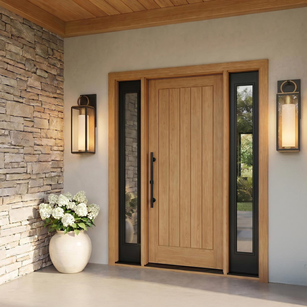 A modern farmhouse entry with glowing matte black and vintage brass wall lanterns flanking a light wood door on stucco, featuring stacked stone and potted white hydrangeas.