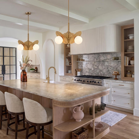 A contemporary kitchen with two brushed brass and opal glass pendants over a curved marble island featuring a fluted white range hood and marble backsplash.