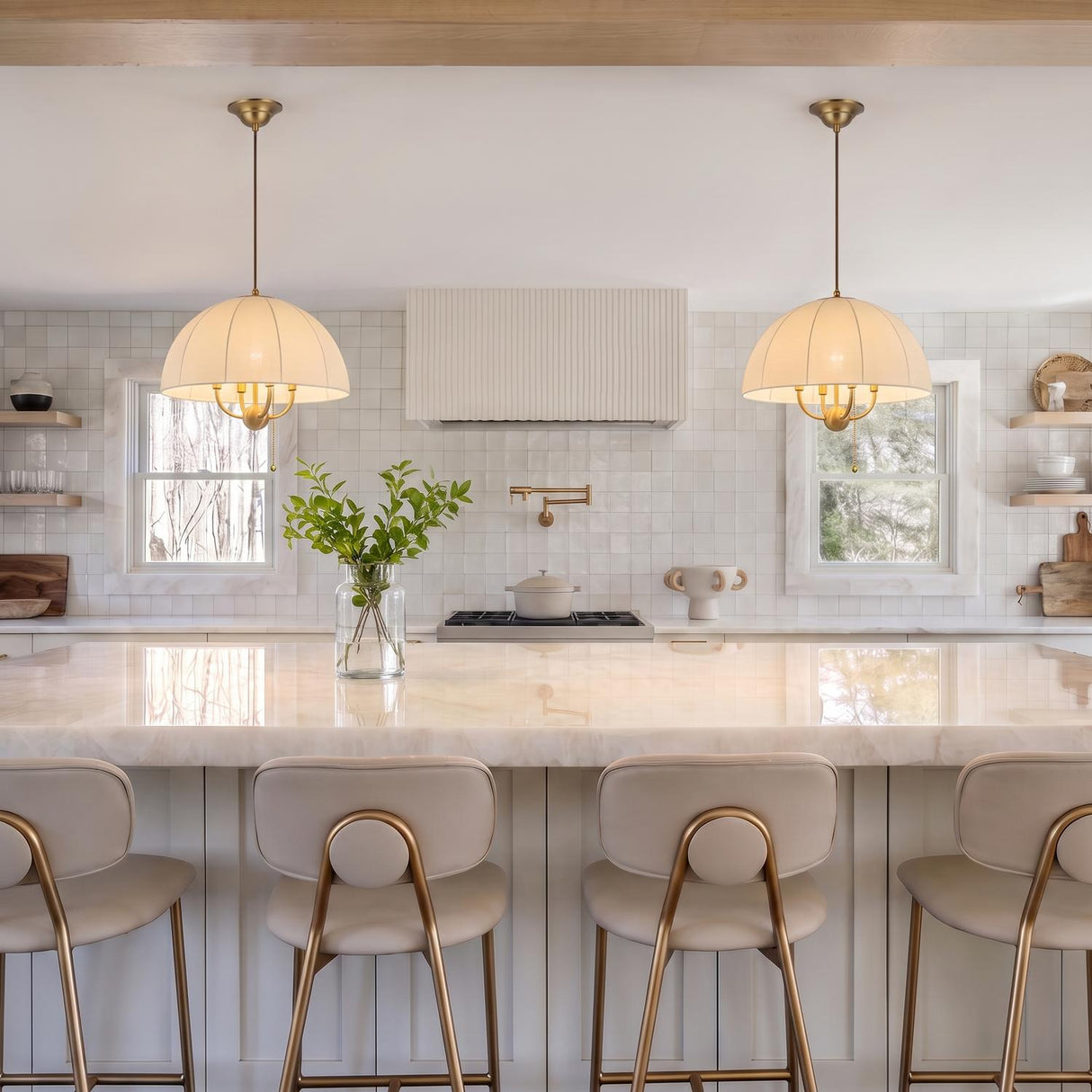 A transitional kitchen featuring two Trudy 4 Light Medium Pendants in brushed brass with fabric shades suspended over a white marble island with beige stools.