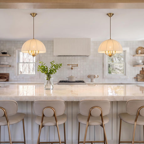 A transitional kitchen featuring two Trudy 4 Light Medium Pendants in brushed brass with fabric shades suspended over a white marble island with beige stools.