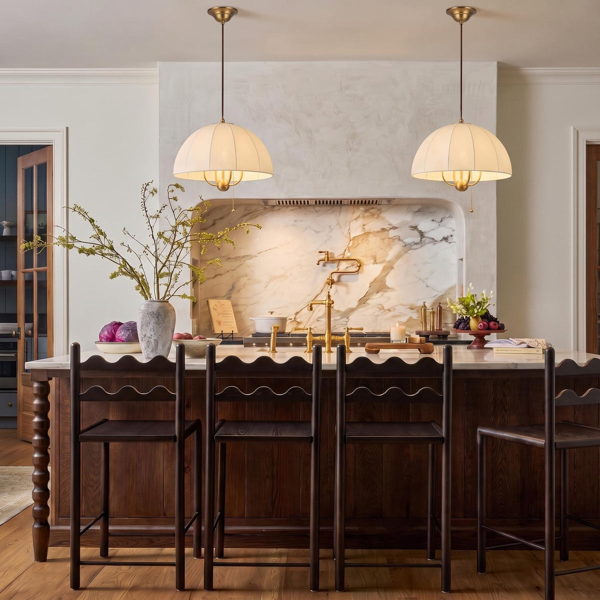 A transitional kitchen with two Trudy 4 Light Medium Pendants in brushed brass with fabric shades hanging over a marble island and dark wood cabinetry.