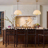 A transitional kitchen with two Trudy 4 Light Medium Pendants in brushed brass with fabric shades hanging over a marble island and dark wood cabinetry.