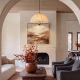 A transitional living room with a matte black fabric shade pendant hanging above a wooden coffee table in front of a stone fireplace.