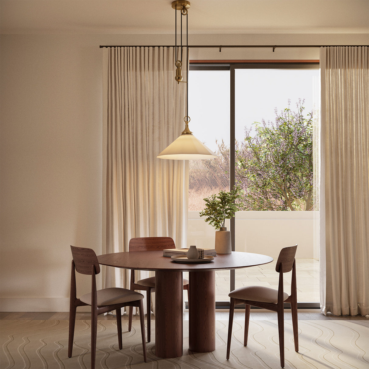 Adele Pendant with Pulley 20", Brushed Brass with Linen Shade, is shown hung above a round dining table with tall linen curtains behind.