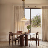 Adele Pendant with Pulley 20", Brushed Brass with Linen Shade, is shown hung above a round dining table with tall linen curtains behind.