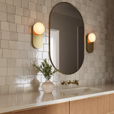 Two Enzo 13" Wall Sconces in Brushed Brass and Opal Glass, flanking a modern oval vanity mirror on handcrafted subway tile wall
