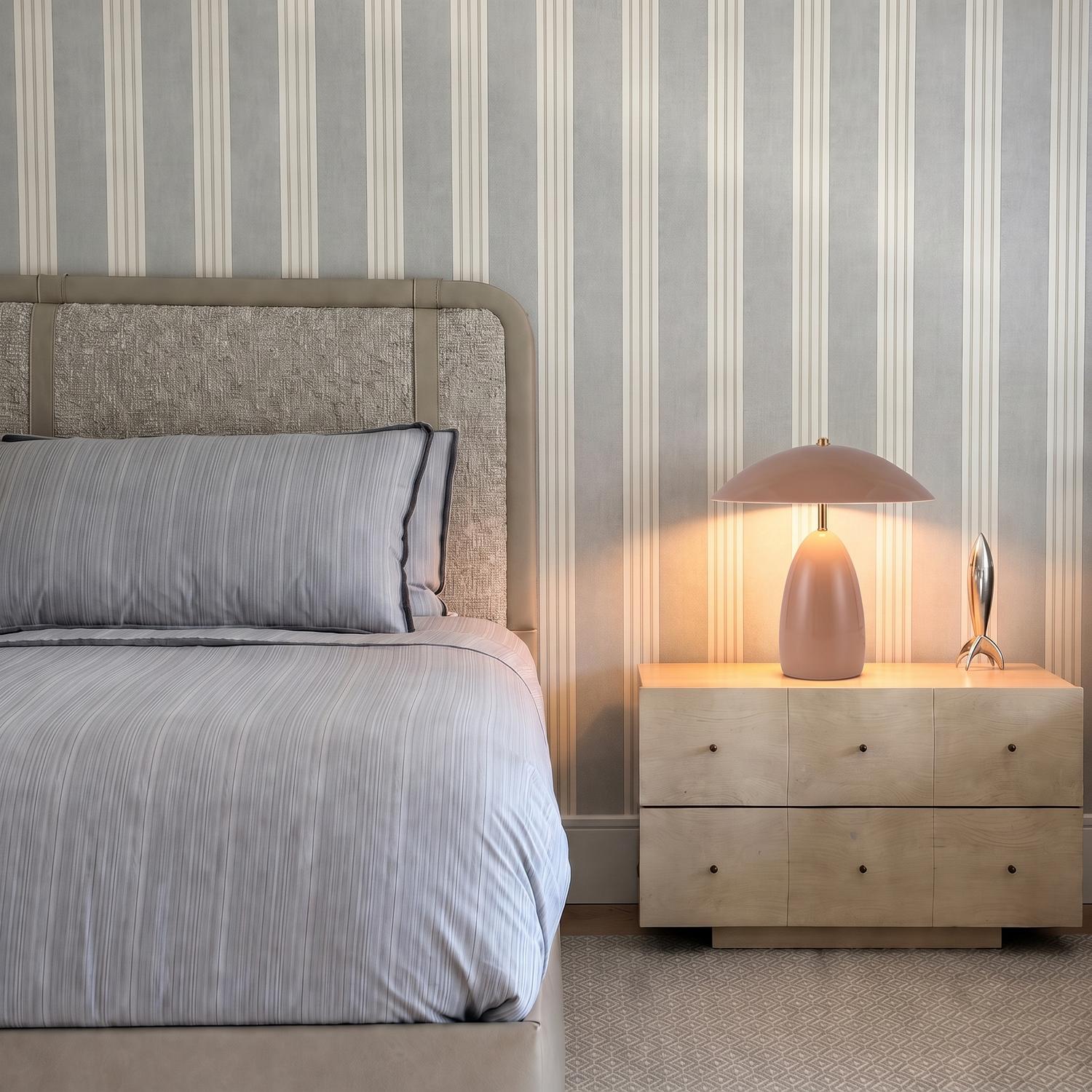 A contemporary bedroom features the Aubrey LED Table Lamp, Blush in a matte blush finish on a light wood nightstand beside a gray upholstered bed.